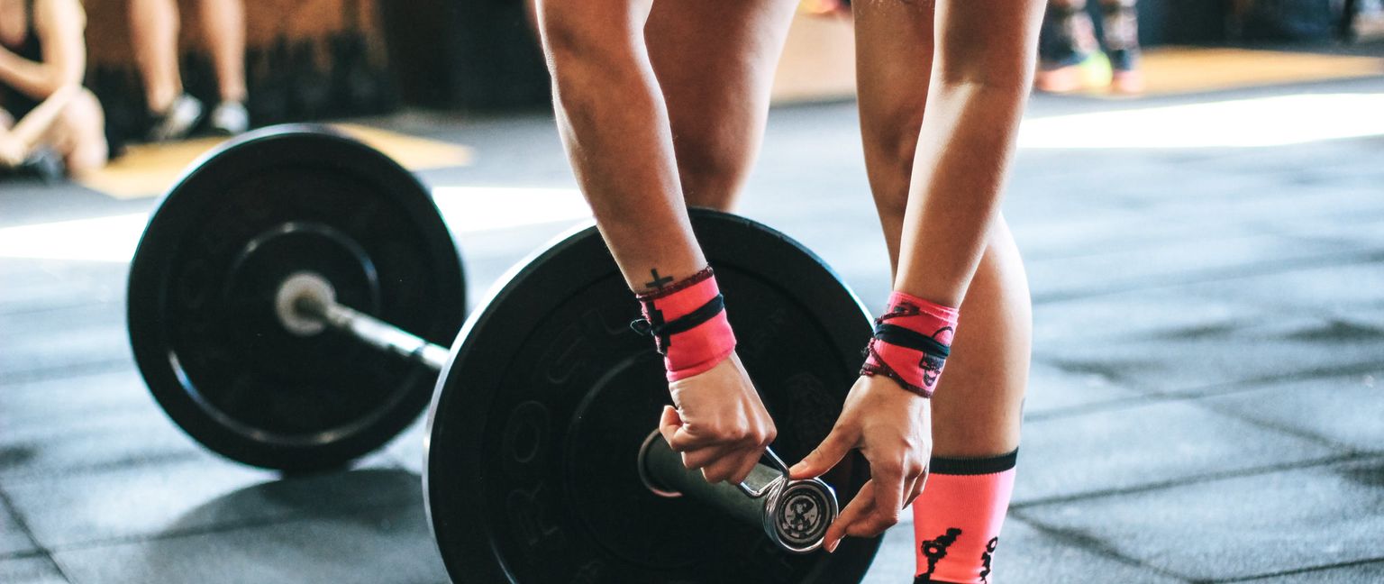 A person adjusts a weight plate on a barbell in a gym. They are wearing pink wrist wraps and socks.