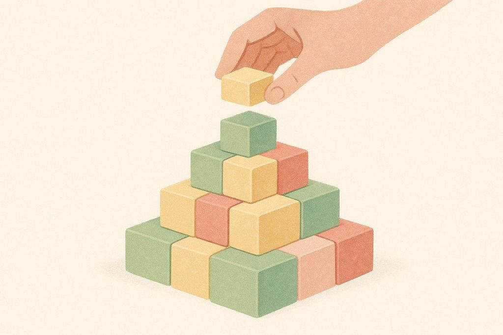 An illustration showing a hand placing a light yellow block on top of a partially constructed pyramid of colorful building blocks, including green, yellow, and red blocks.