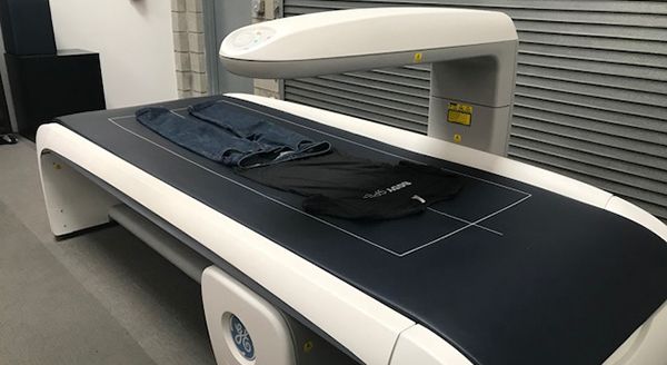 Jeans and a black t-shirt lying flat on the surface of a large white GE medical scanner.